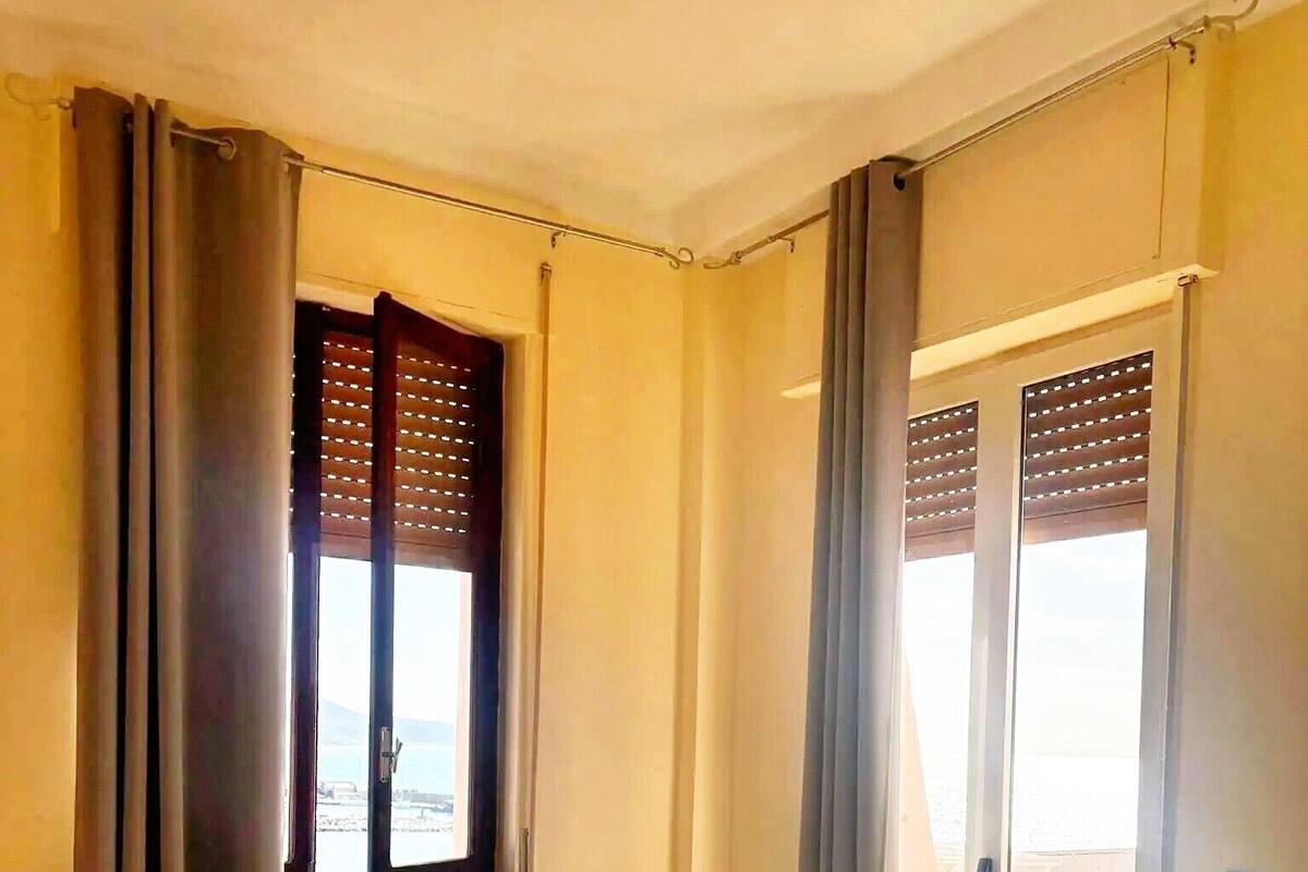 Une chambre d’hôtel avec un lit, une fenêtre avec des stores, une porte donnant sur une vue agréable et un balcon.