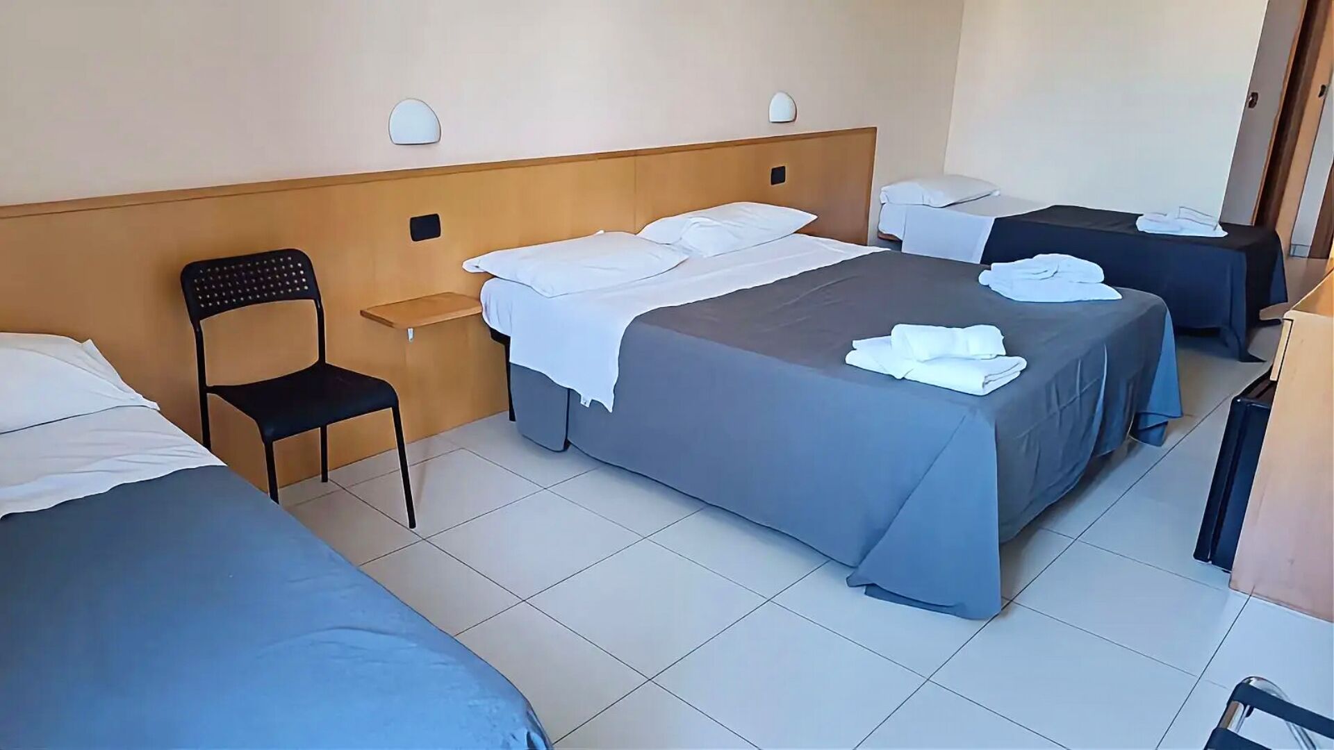 Ein Hotelzimmer mit zwei Betten, einem Sessel, einem kleinen Tisch und einem Schreibtisch mit Stuhl.