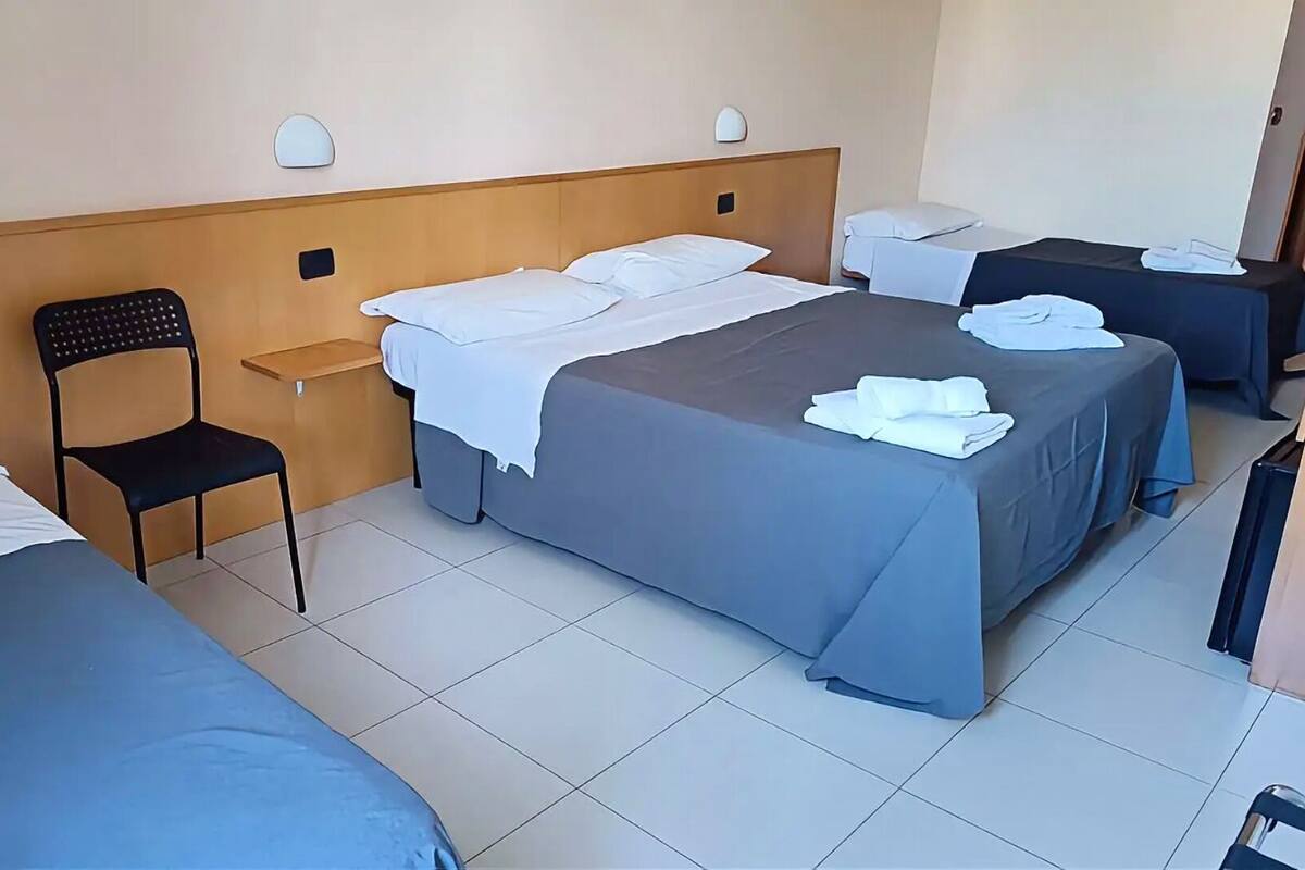 Une chambre d’hôtel avec deux lits simples, une chaise, une petite table et un bureau avec une chaise.