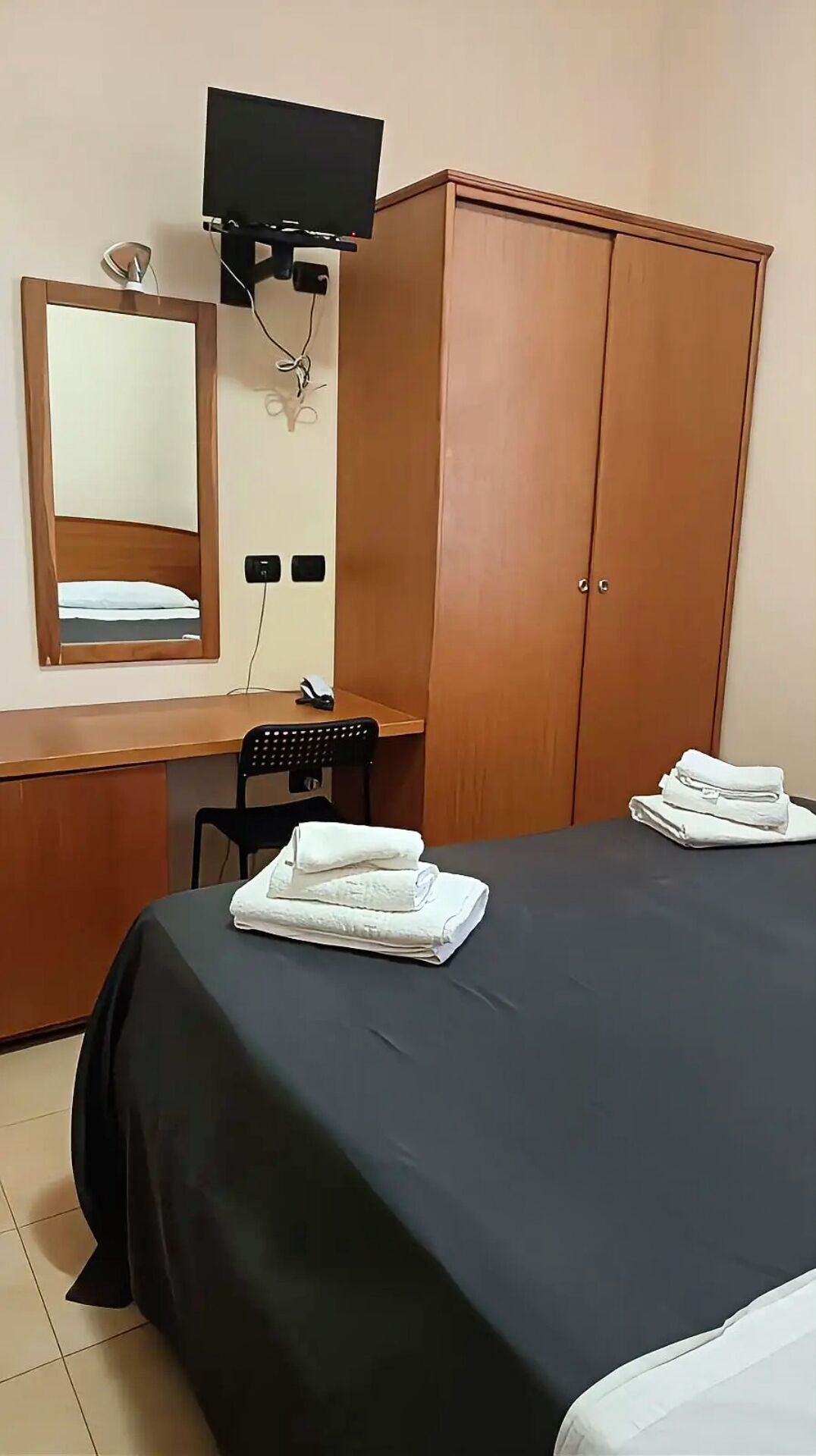 Ein Hotelzimmer mit Bett, Schreibtisch, Stuhl, Kleiderschrank, Fernseher und Spiegel.