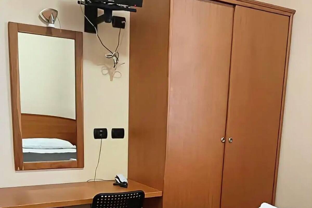 Une chambre d’hôtel équipée d’un lit, d’un bureau, d’une chaise, d’une armoire, d’une télévision et d’un miroir.