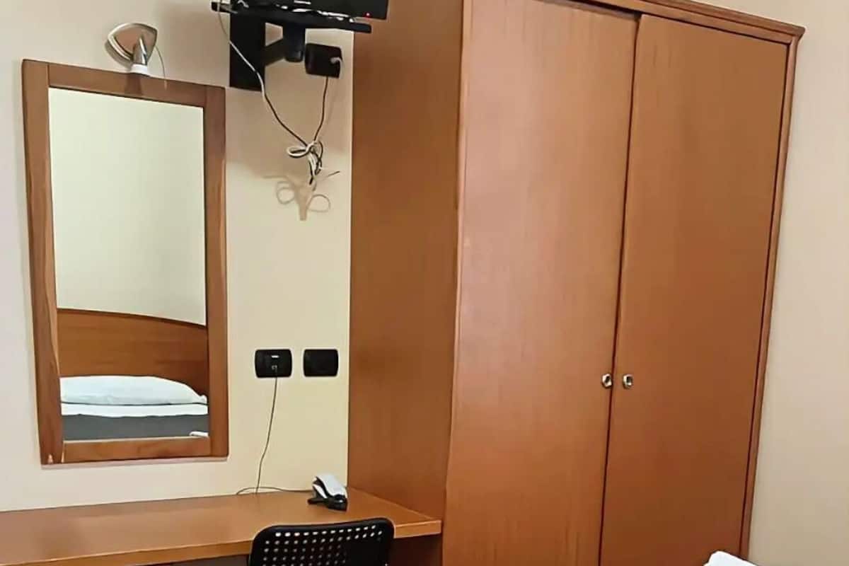 A hotel room with a bed, a desk, a chair, a wardrobe, a television, and a mirror.