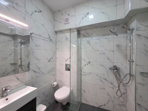 Ein modernes Badezimmer mit Marmorwänden, einer Duschkabine aus Glas, einem weißen Waschbecken und einer Toilette.