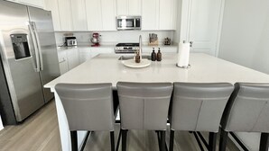 A modern kitchen with white cabinets, stainless steel appliances, a central island with bar stools, and a microwave above the stove. - New spacious 4-bedroom house in serene Brighton with cool AC and fast Wi-Fi. (Brighton)