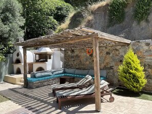 Eine Terrasse mit einer Holz-Pergola, einer Steinmauer und einem grünen Nadelbaum.