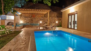 A swimming pool with a wooden deck, lounge chairs, and a stone wall. - Pura Vida (Agios Vasileios)