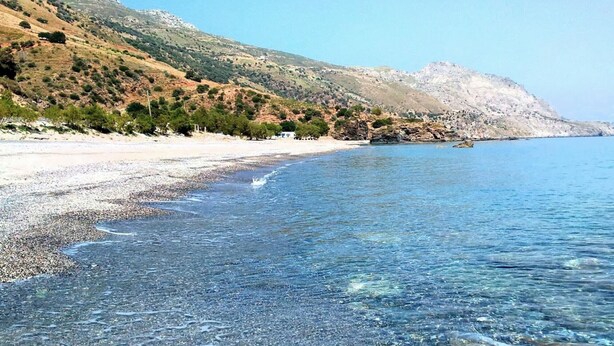 A beach with clear water, pebbles, and a hillside with sparse vegetation. - Pura Vida (Agios Vasileios)