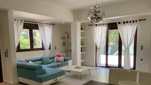 A modern living room with a teal sofa, a white coffee table, and a dining area with a black table and white chairs. - Pura Vida (Agios Vasileios)
