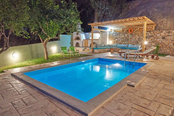 Ein Schwimmbecken mit Holzterrasse und Liegestühlen, umgeben von Steinmauern und einer Pergola.