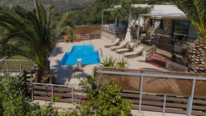 A pool area with lounge chairs, a stone building, and a view of mountains. - Souda Bay Cottage (Agios Vasileios)