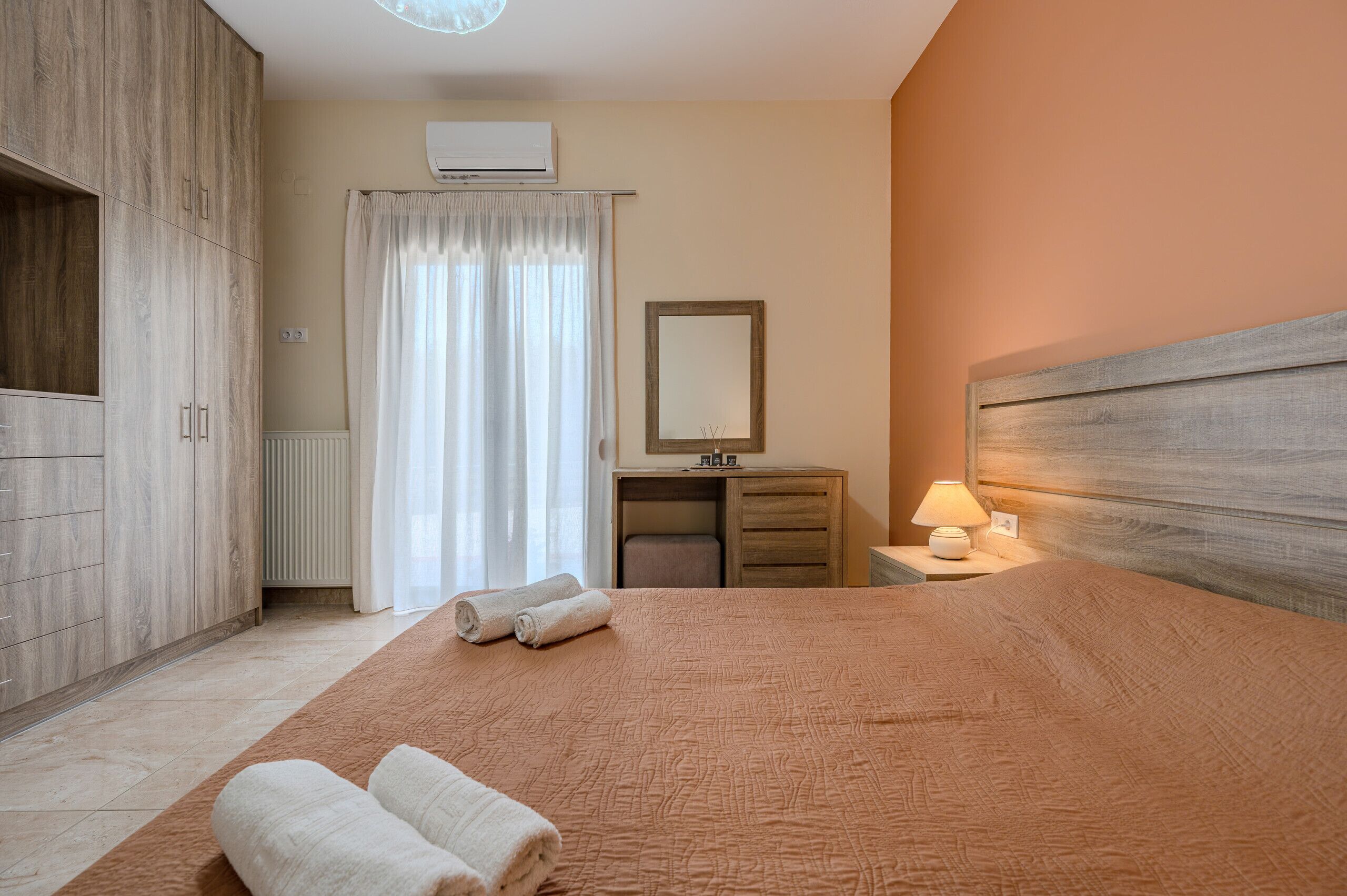 A bedroom with a bed, a nightstand, a dresser, a mirror, and a window with curtains.