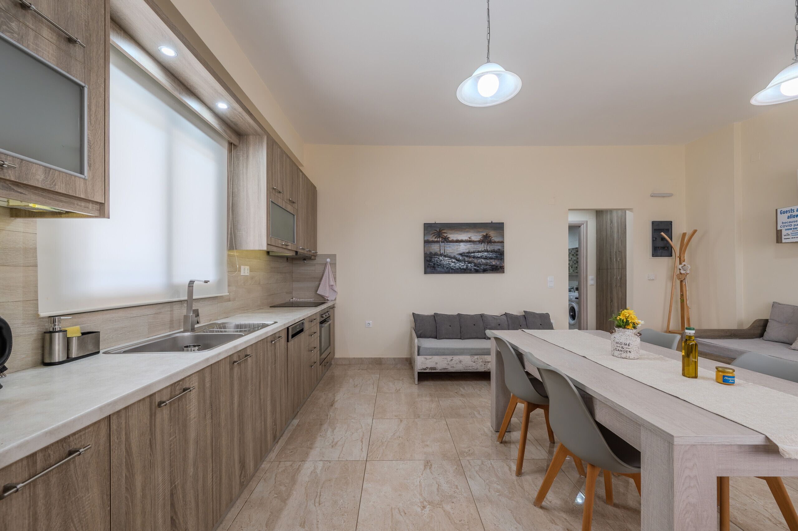 A modern kitchen with wooden cabinets, a large window, and a dining area with a sofa and table.