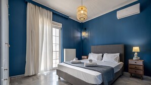 A bedroom with a large bed, a bedside table with a lamp, a window with curtains, and an air conditioning unit on the wall. - Platanias Villa Spyros (Rethymno)