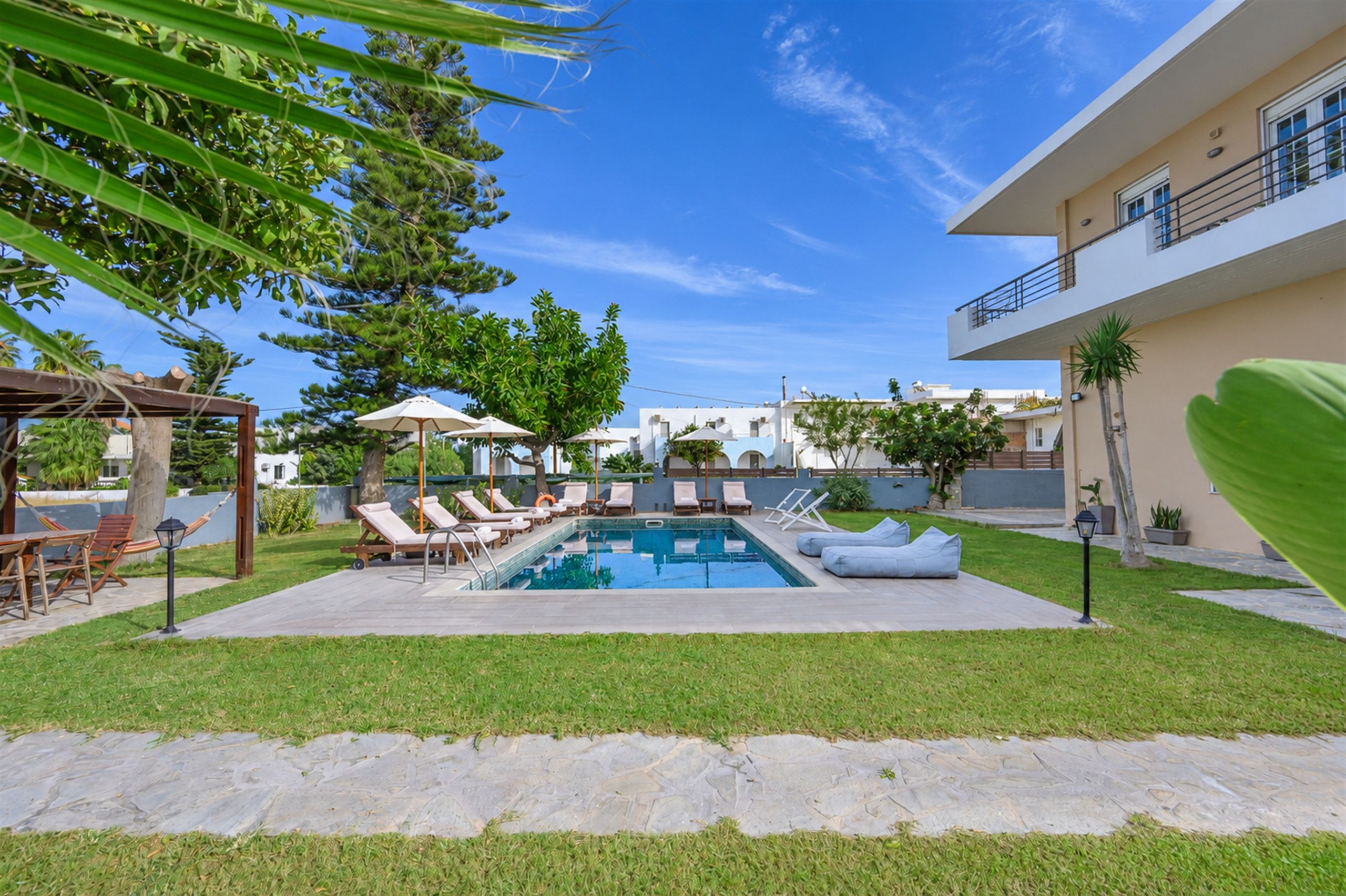 A swimming pool with lounge chairs and umbrellas, surrounded by a well-maintained lawn and a building with balconies.