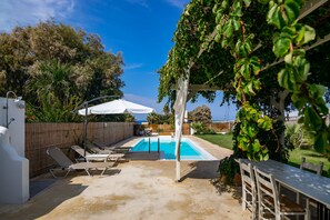 Een zwembad met ligbedden, een pergola begroeid met klimplanten en uitzicht op de zee.