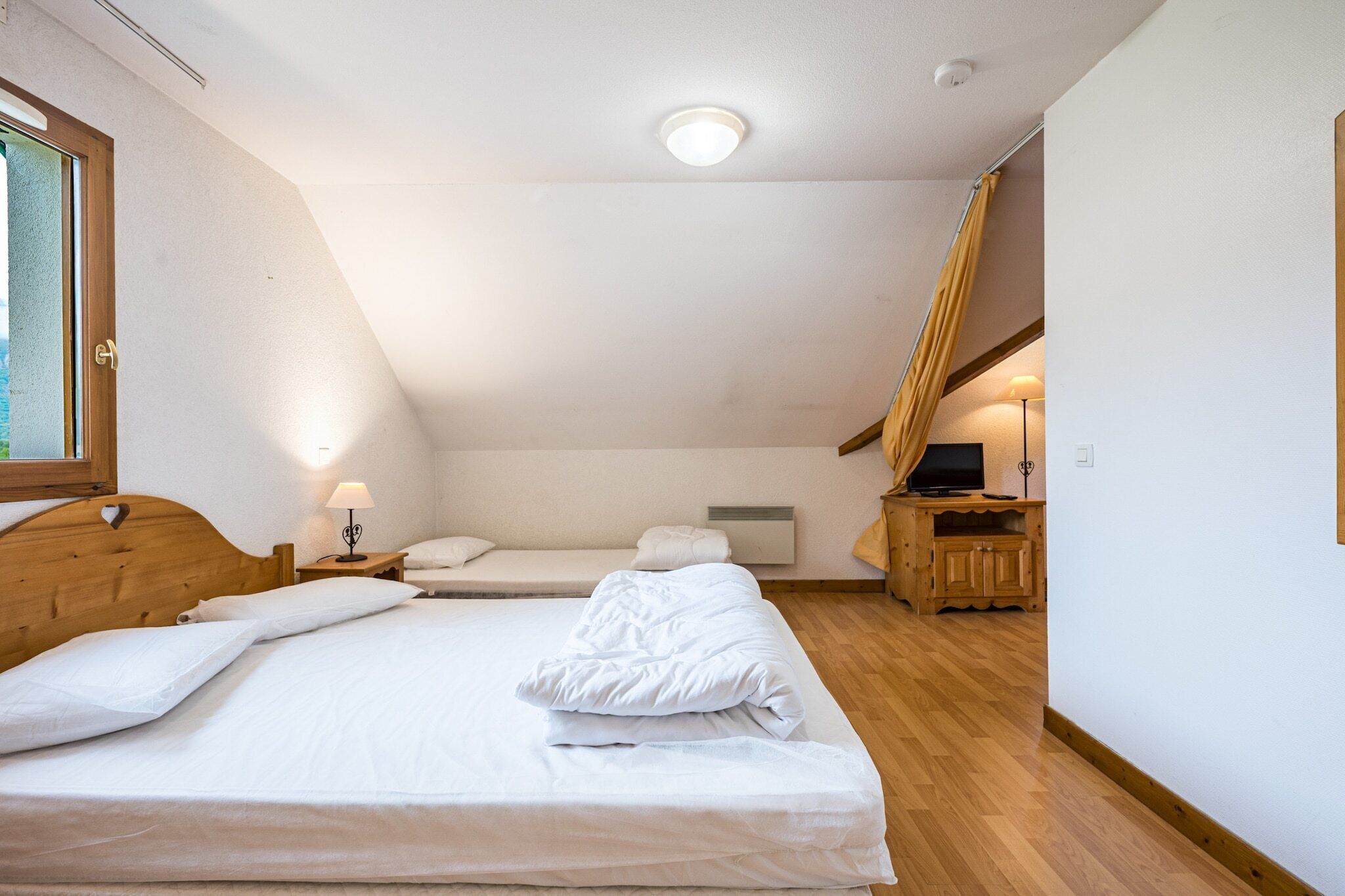 Ein Schlafzimmer mit einem großen Bett, einem kleineren Bett, einem Schreibtisch und einem Fenster.
