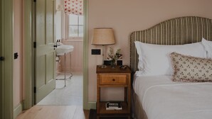 Ein Schlafzimmer mit Bett, Nachttisch, Lampe und Blick ins Badezimmer.
