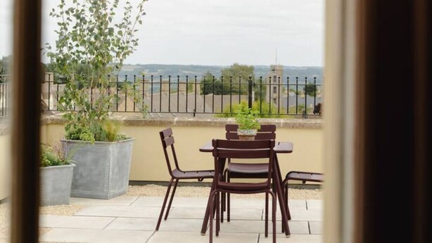Eine Terrasse mit Tisch und Stühlen, Blumentöpfen und Blick auf die Landschaft hinter einem Zaun.