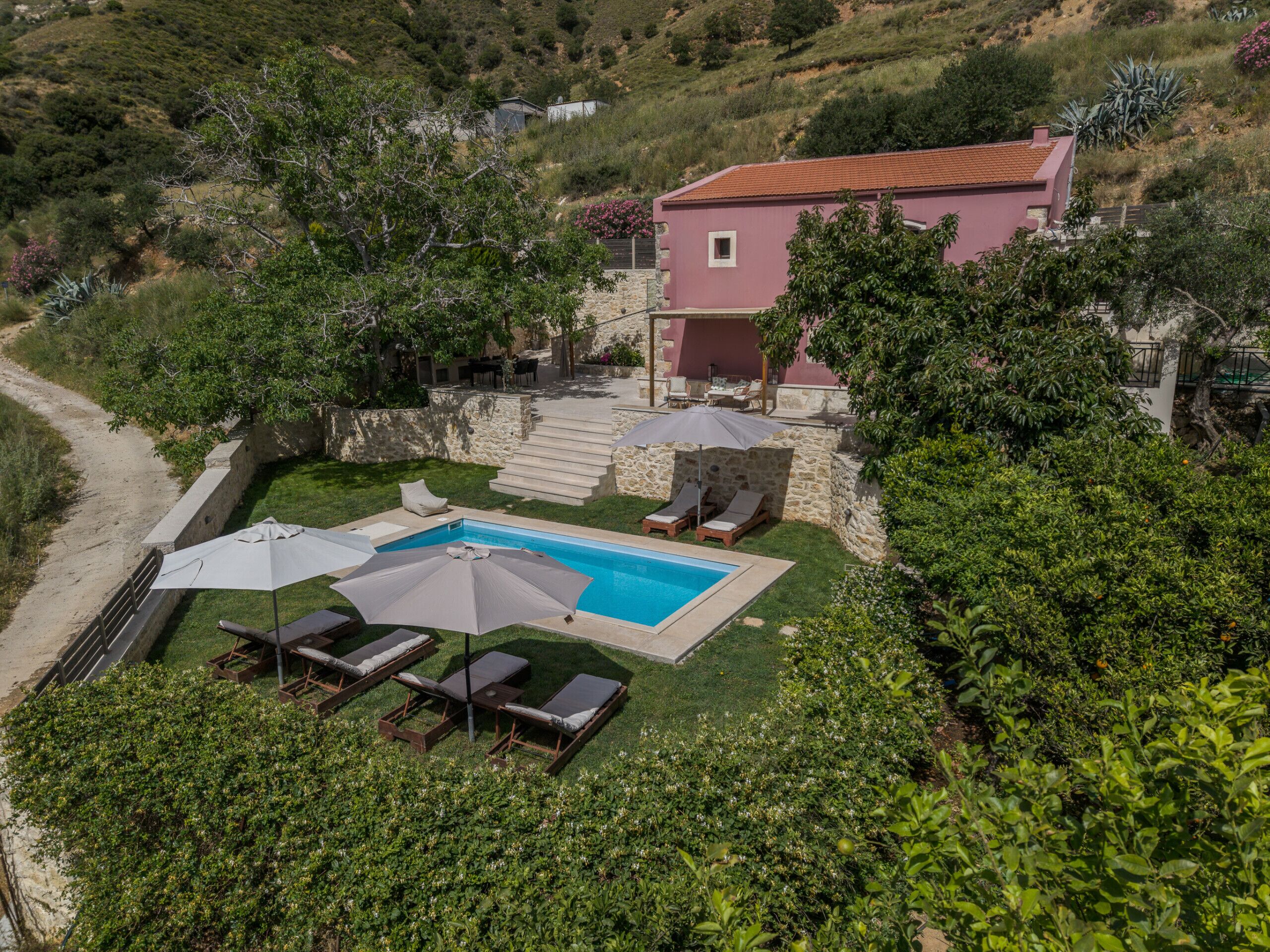 A hillside villa with a swimming pool, outdoor seating, and a stone staircase.