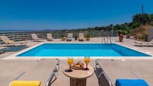 Una piscina con sillas de descanso y una mesa con bebidas y aperitivos.
