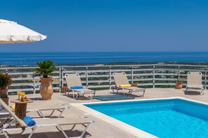 A pool area with lounge chairs and a view of the ocean. - Haravgi Villa (Rethymno)