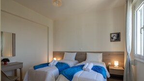 Una habitación de hotel con dos camas, un escritorio, una mesita de noche con lámpara y una ventana con cortinas.