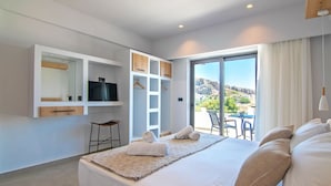 Ein modernes Hotelzimmer mit einem großen Bett, einem Fernseher, einem Kleiderschrank und einem Balkon mit Blick auf die Hügel.