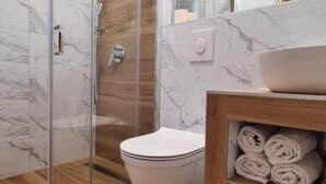 Un baño moderno con cabina de ducha de vidrio, inodoro blanco y tocador de madera con lavabo y toallas.
