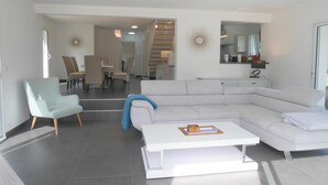Ein modernes Wohnzimmer mit einem hellen Ecksofa, einem weißen Couchtisch und einem hellblauen Sessel.