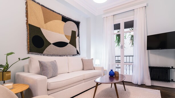 A modern living room with a sofa, a coffee table, a large abstract painting, and a TV mounted on the wall. - Athens Heart Gem Lux Apartment (Athens)