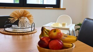 Une table à manger avec un set de table en fibres tressées, un bocal en verre, un objet décoratif et un saladier rempli de fruits.