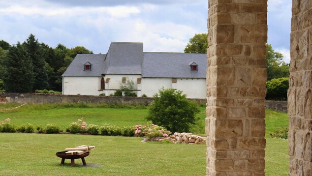 Un pilier de pierre et un bâtiment blanc avec un toit gris, situés dans une zone herbeuse.