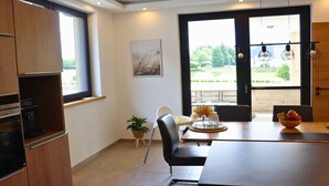 Une cuisine moderne dotée d’un four encastré, un coin repas avec une table et des chaises, et une grande fenêtre offrant une vue sur la verdure.