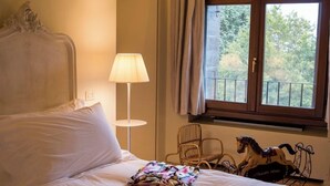 Une chambre d’hôtel avec un lit, une lampe, une fenêtre avec des rideaux et un chariot à cheval décoratif.