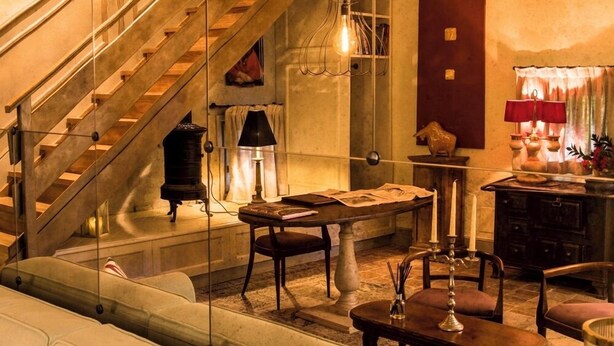 Une pièce chaleureuse avec un escalier en bois, une table décorée de bougies et une lampe d’époque.