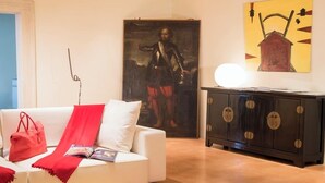 Un salon moderne avec un canapé blanc, des accessoires rouges, un meuble noir doté de poignées rondes et un tableau accroché au mur.