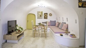 A living room with a TV, dining table, chairs, a sofa, and a small bookshelf. - Areopolis Art Apartment (East Mani)