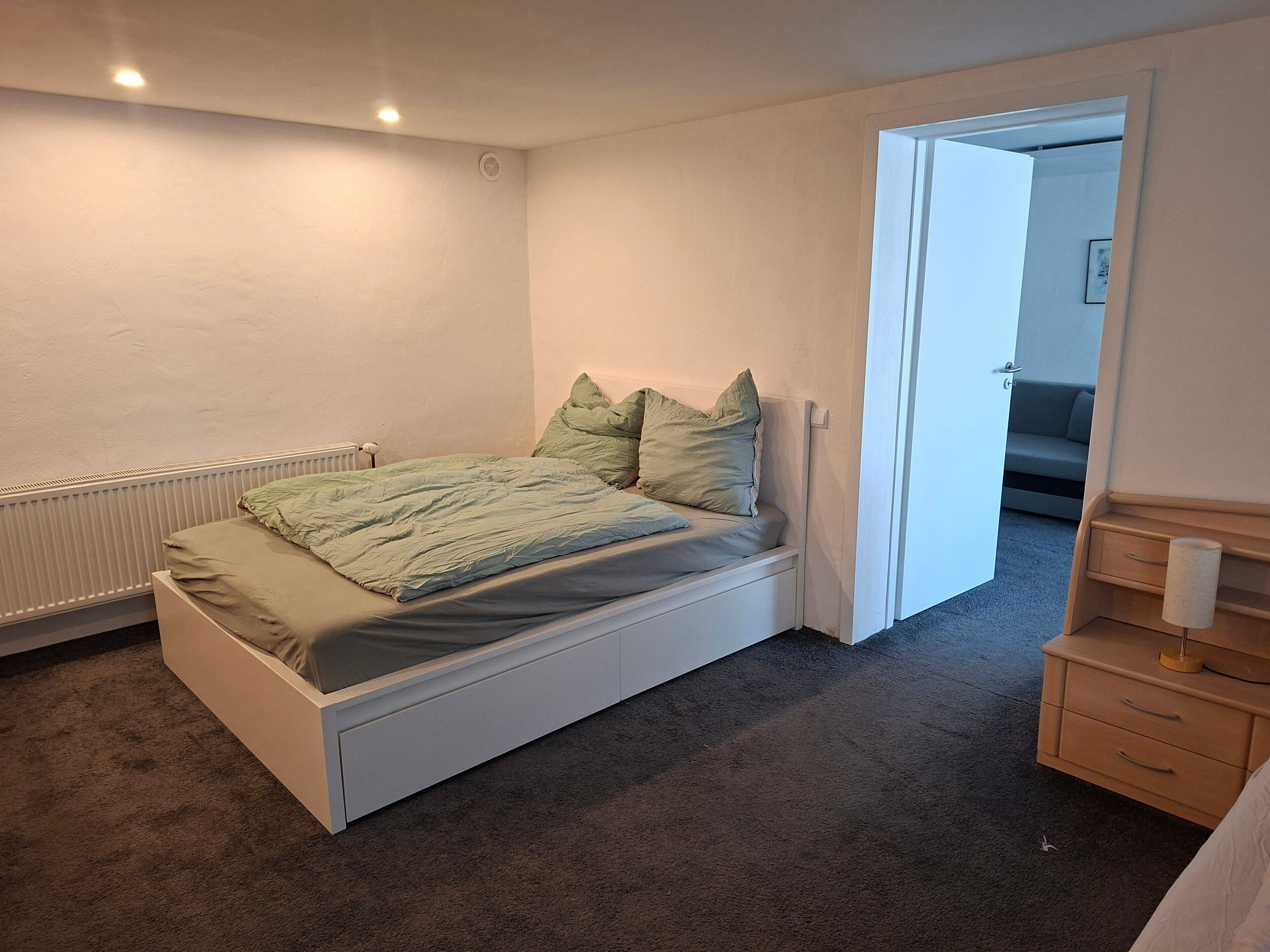 Ein Schlafzimmer mit einem Bett, einem Heizkörper, einem Schminktisch und einer Tür zu einem anderen Raum.