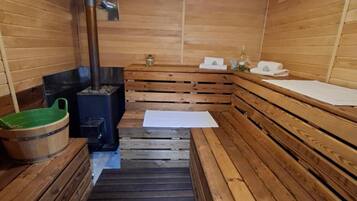 A sauna room with wooden benches, a bench heater, a bucket, and a towel rack.
