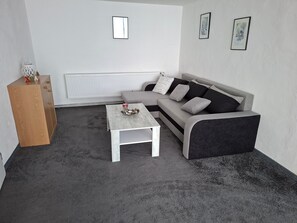 Un salon moderne avec un canapé gris, une table basse blanche, un meuble en bois et un radiateur.