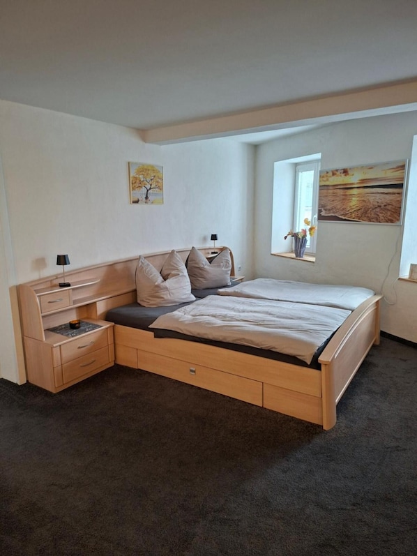 Une chambre à coucher avec un lit, des tables de chevet, une fenêtre et des œuvres d’art accrochées aux murs.