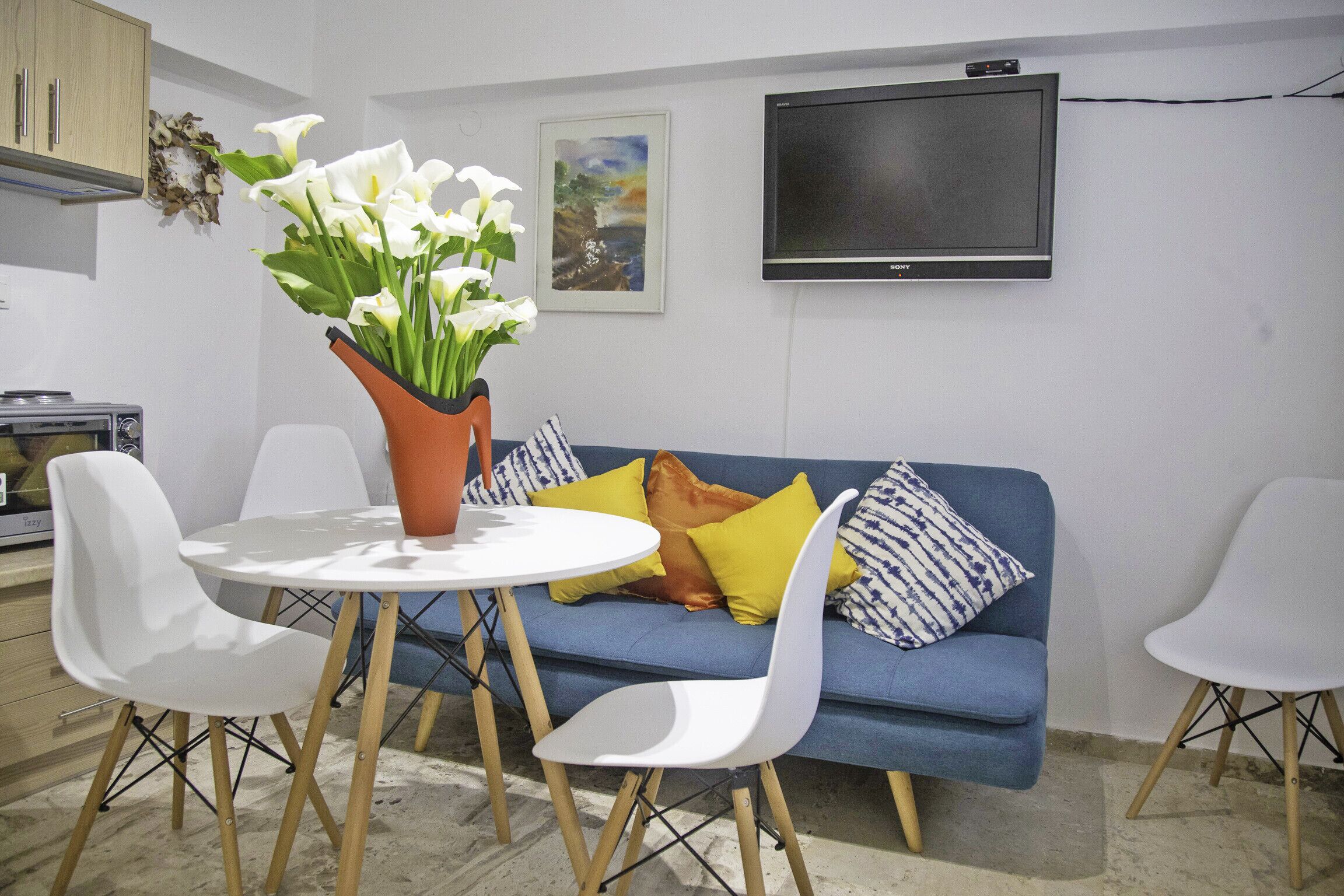 Un salon moderne avec un canapé bleu, des fauteuils blancs, une table ronde et un vase rempli de fleurs blanches.