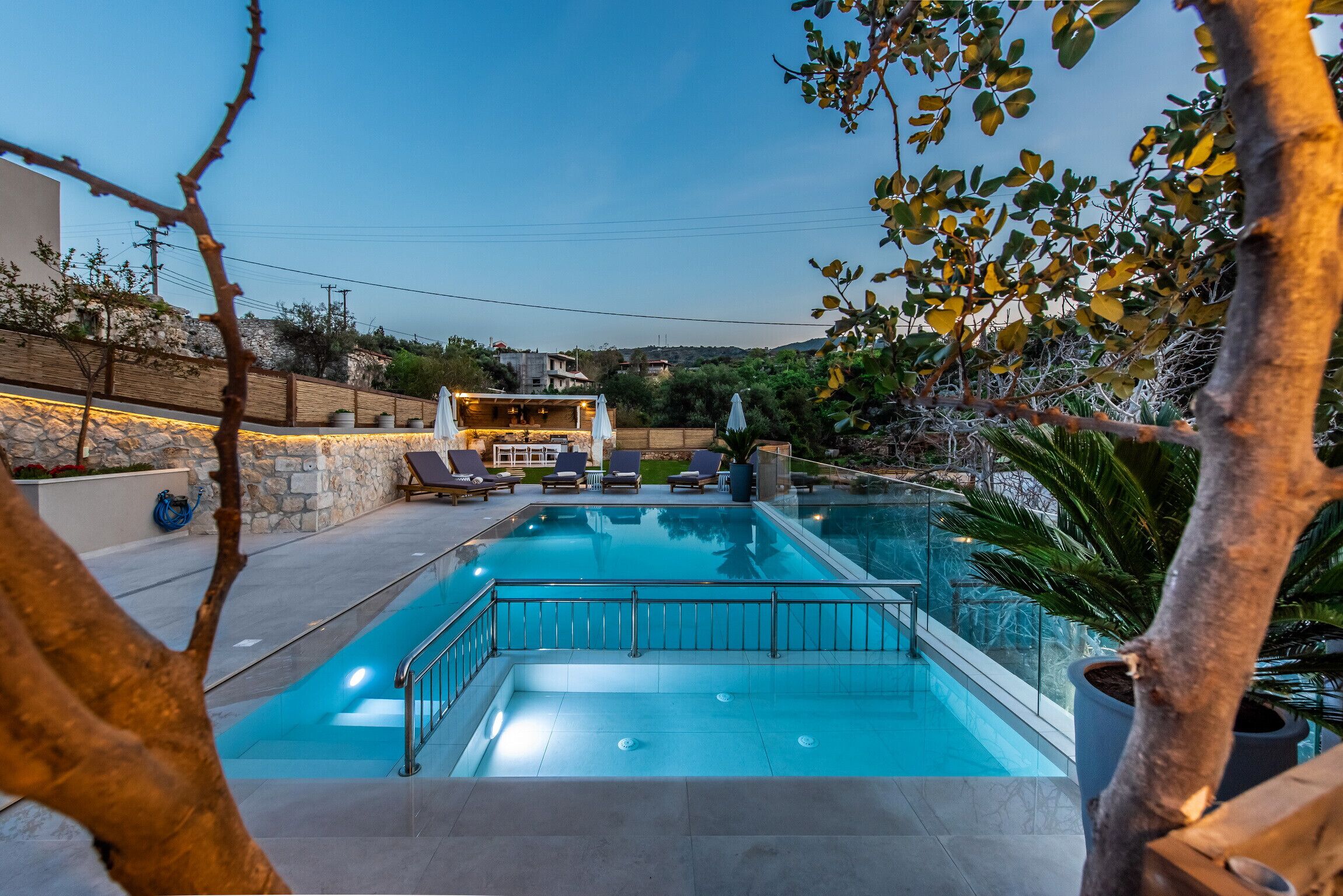 A swimming pool with lounge chairs and a covered seating area, surrounded by stone walls and greenery.