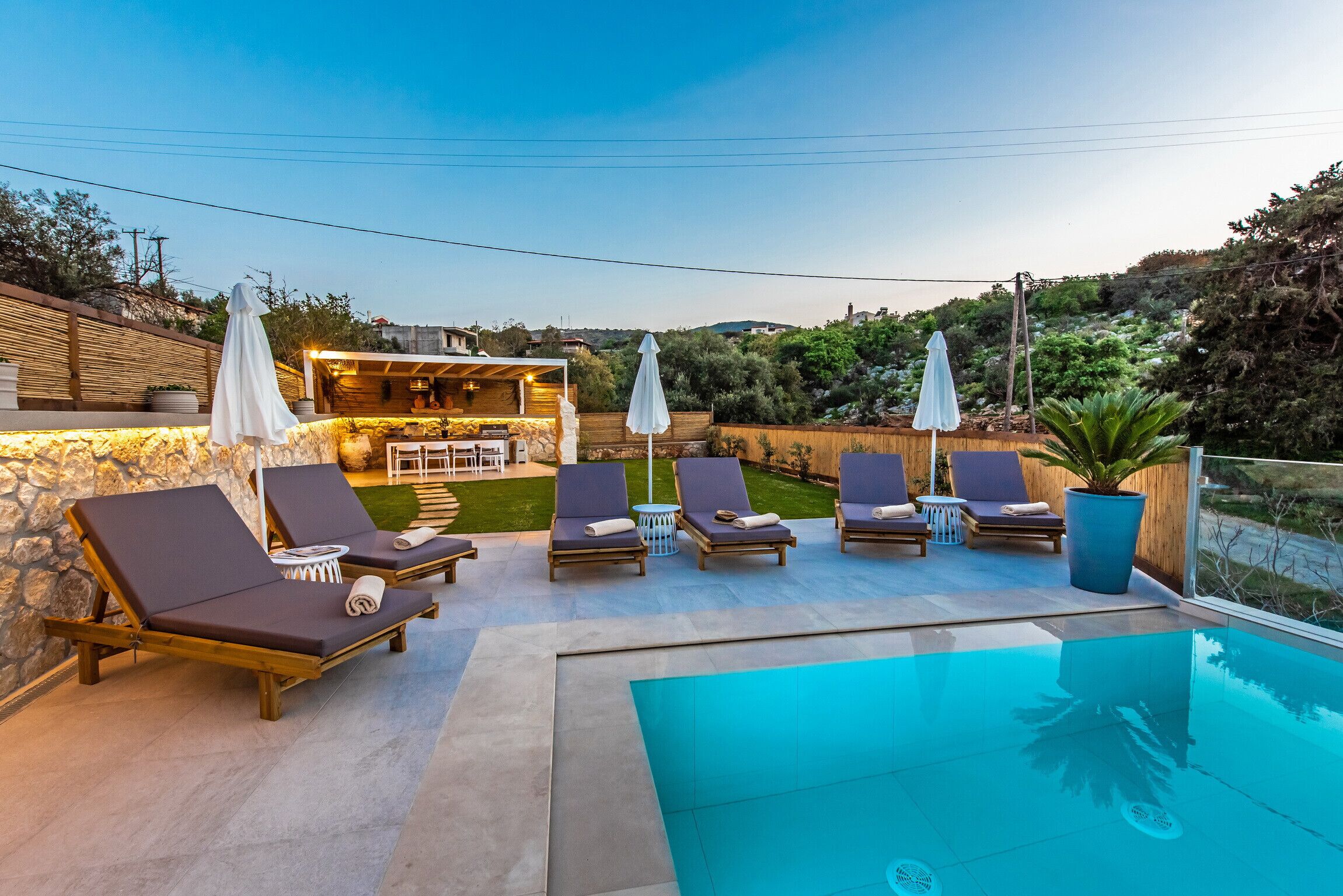 A poolside area with lounge chairs and umbrellas, a stone wall, and a wooden deck.
