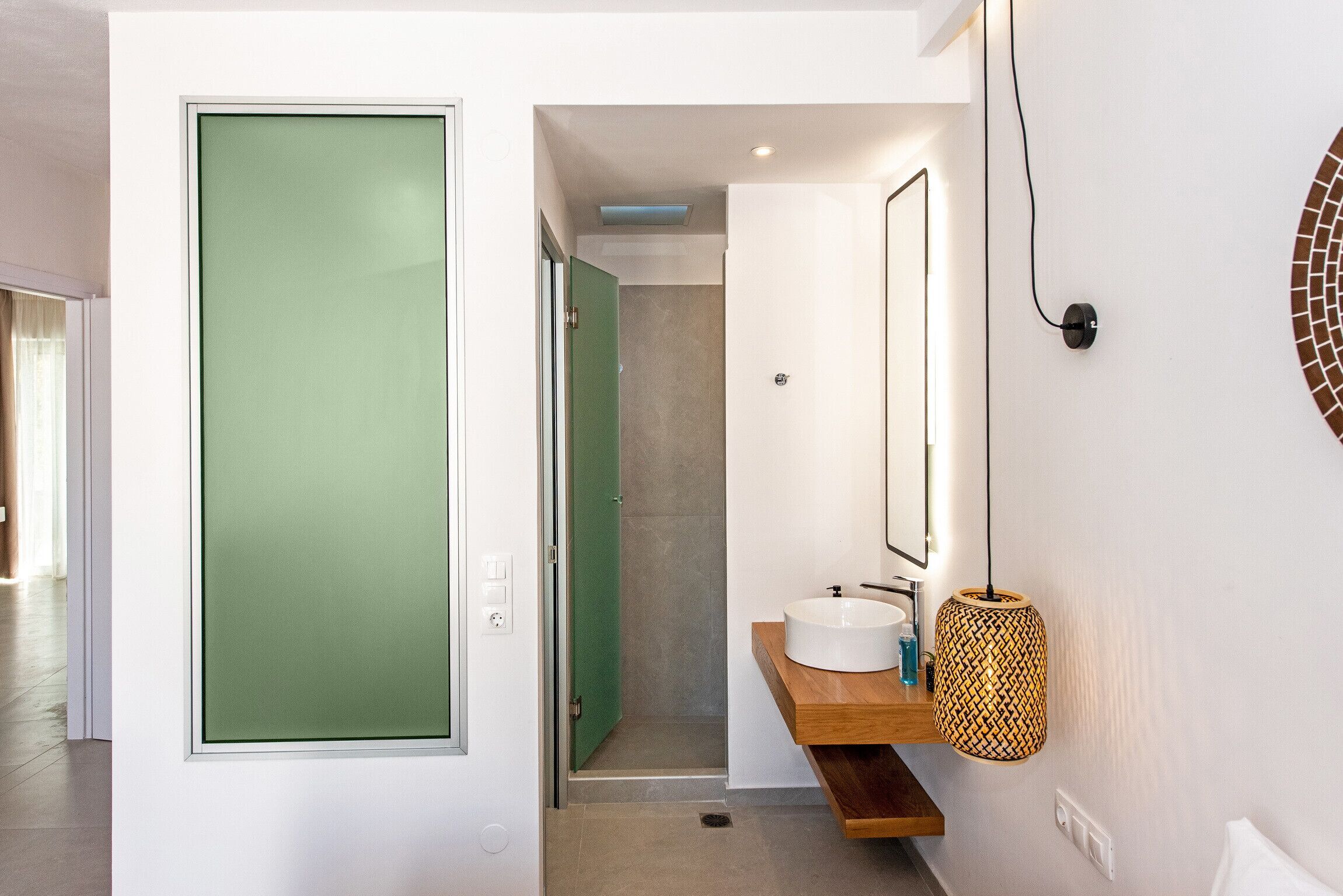 Une salle de bain moderne avec une porte en verre dépoli vert, un lavabo blanc et un meuble-lavabo en bois.