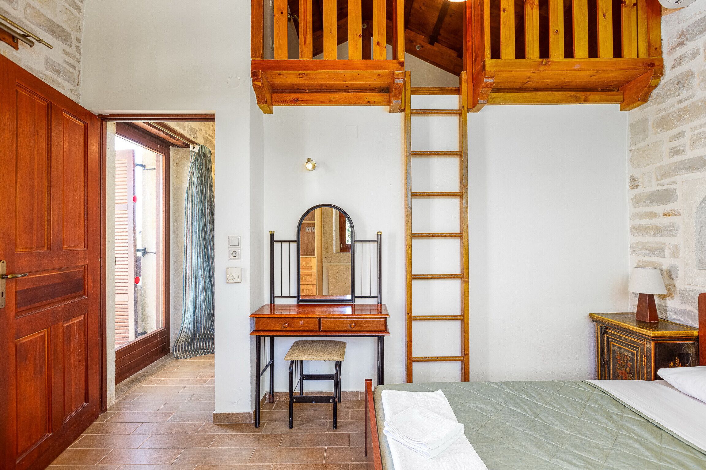 A bedroom with a wooden desk, a ladder, a bed, and a nightstand.