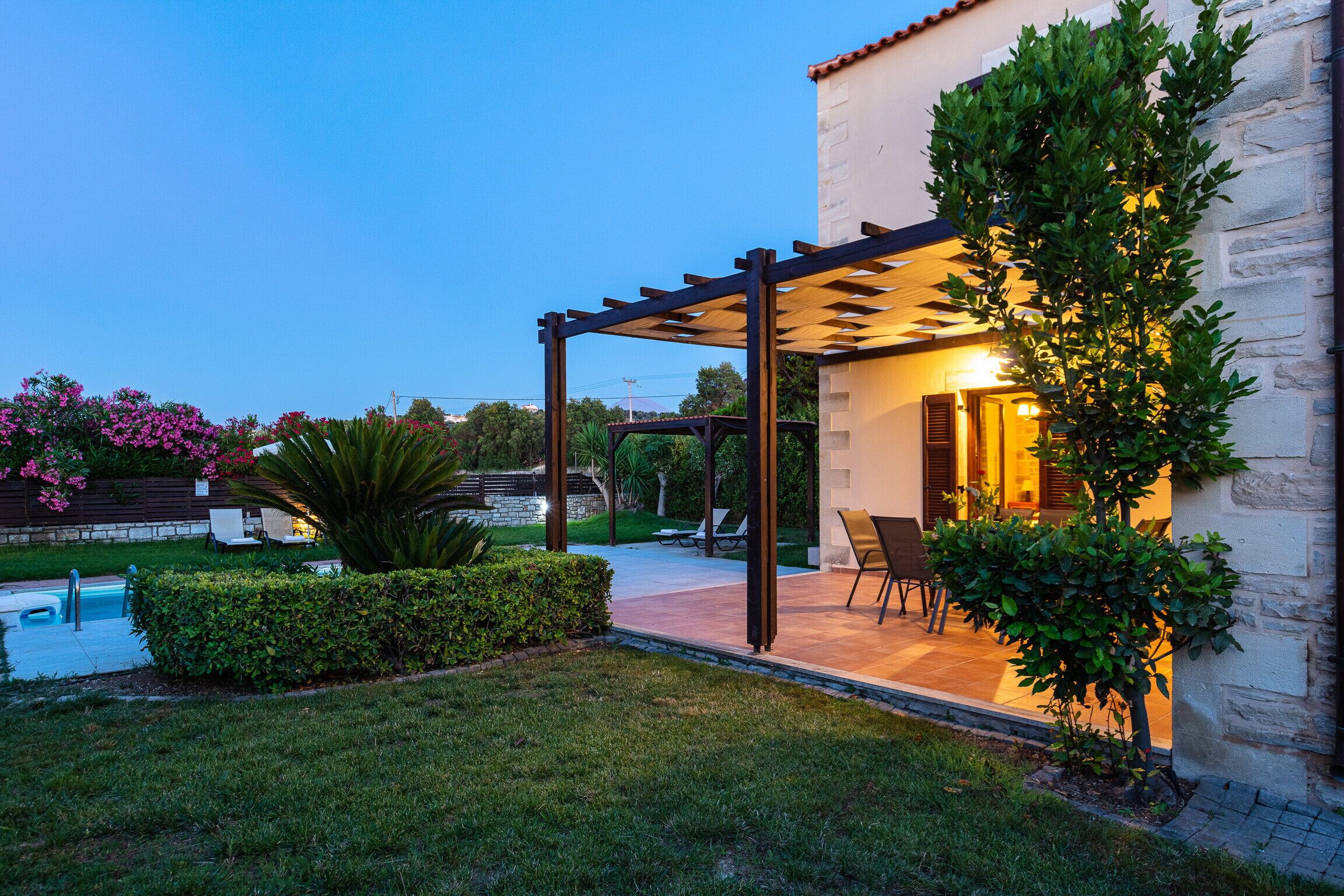 A covered outdoor patio with a pool, seating area, and a stone building.