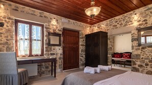 A stone-walled room with a bed, a desk, a chair, and a wooden ceiling. - Archodiko Villa Imbros (Sfakia)