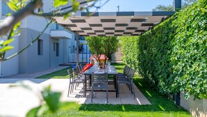 Een terras met een tafel voor vier personen, omringd door stoelen, onder een geruit afdak.
