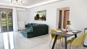 Een moderne woonkamer met een groene bank, een eettafel met gele stoelen en een schilderij aan de muur.